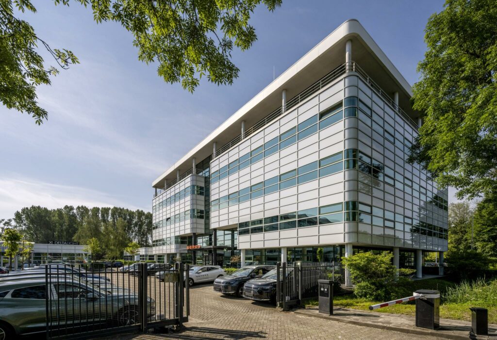 Modern kantoorgebouw aan de Burgemeester Stramanweg met glazen gevel en parkeerplaats op de voorgrond.